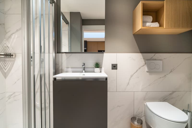 Modern bathroom with marble-like tiles, glass shower enclosure, vanity with sink, storage cabinet, and toilet