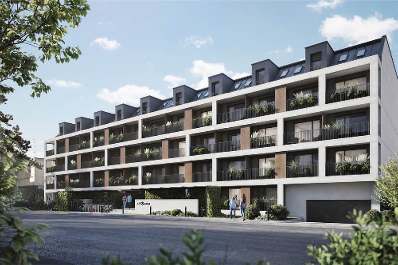 Multi-story apartment building with balconies, modern architectural design, and greenery surrounding the building.