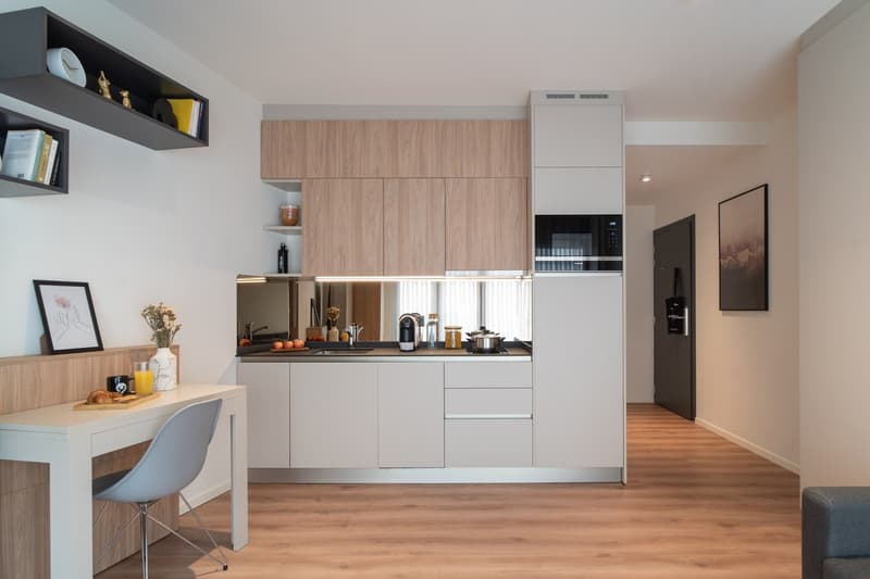 Modern kitchen with light wood cabinets, white appliances including a dishwasher, and a small dining area with a table and chair.