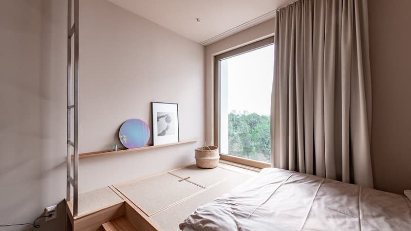 Bedroom with bed, bedside table, shelf, window with view to outside, wall-mounted mirror, woven basket.
