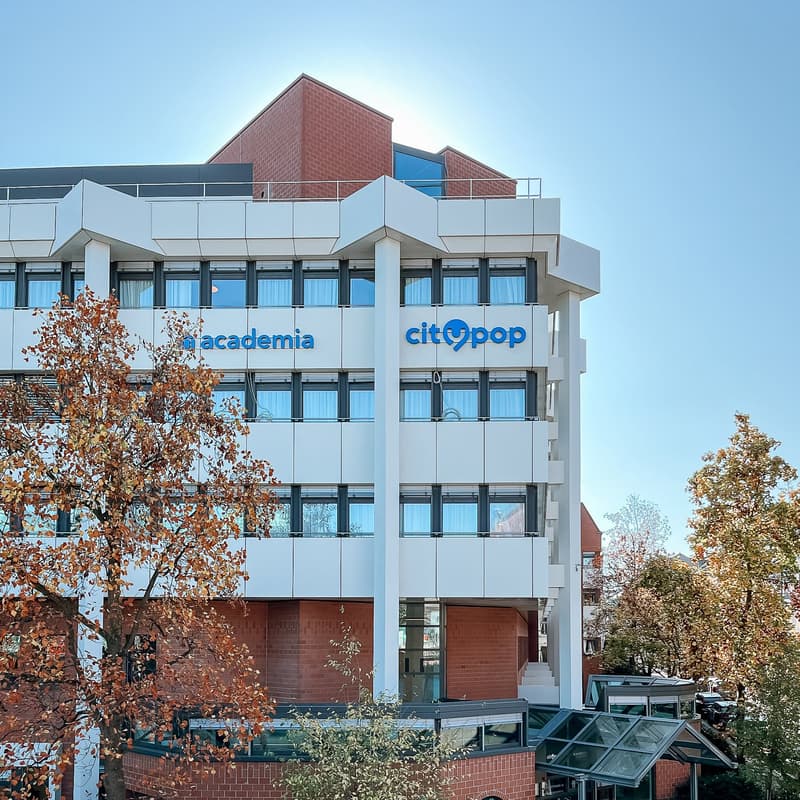 A multi-story office building with a modern, glass-and-brick facade. The building has balconies on some floors and the Citypop and Academia logos are visible on the exterior.