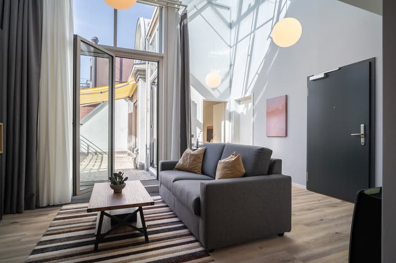 Spacious living room with large windows, gray sofa, wooden coffee table, striped rug, and balcony access