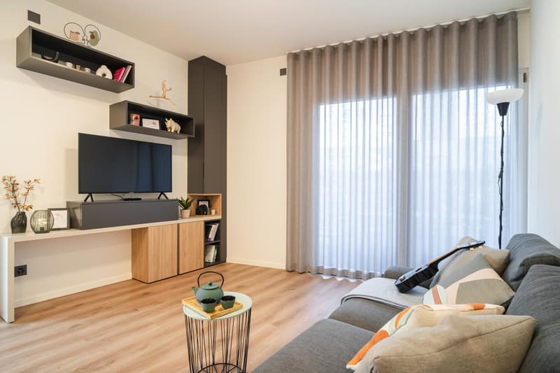 Minimalist decor, wooden floor, large windows with curtains, TV unit, couch, center table, lamp