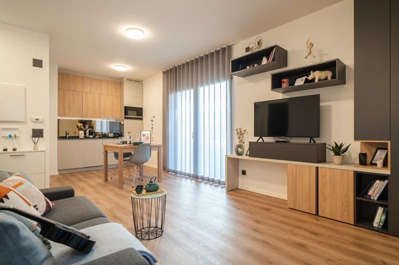 modern open plan living room, wooden floor, gray couch, wooden dining table, TV on entertainment unit, open kitchen with breakfast bar