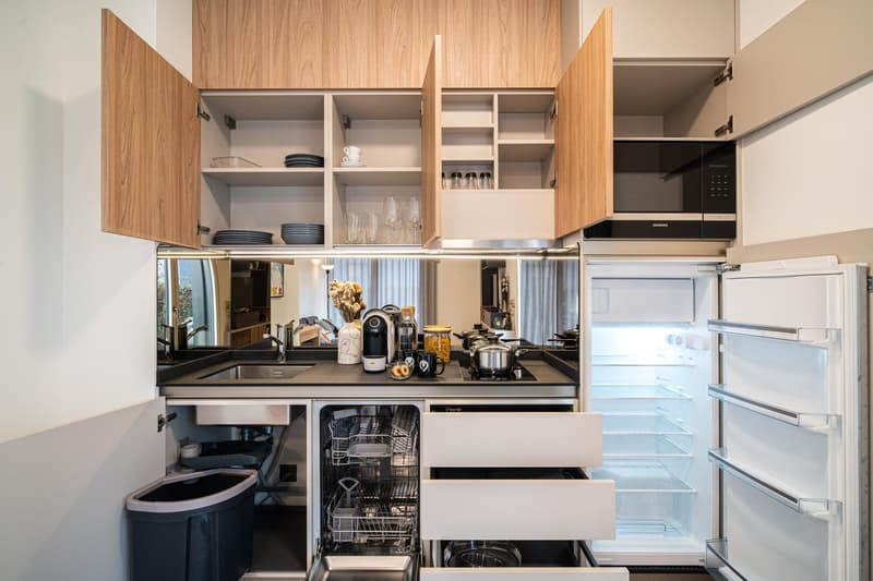 Modern kitchen with wooden cabinets, open drawers, open refrigerator, built-in dishwasher, and open cabinet doors.