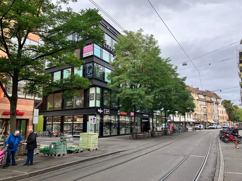 large store building with many signs and windows, street lamps, people, parked bicycles, trees