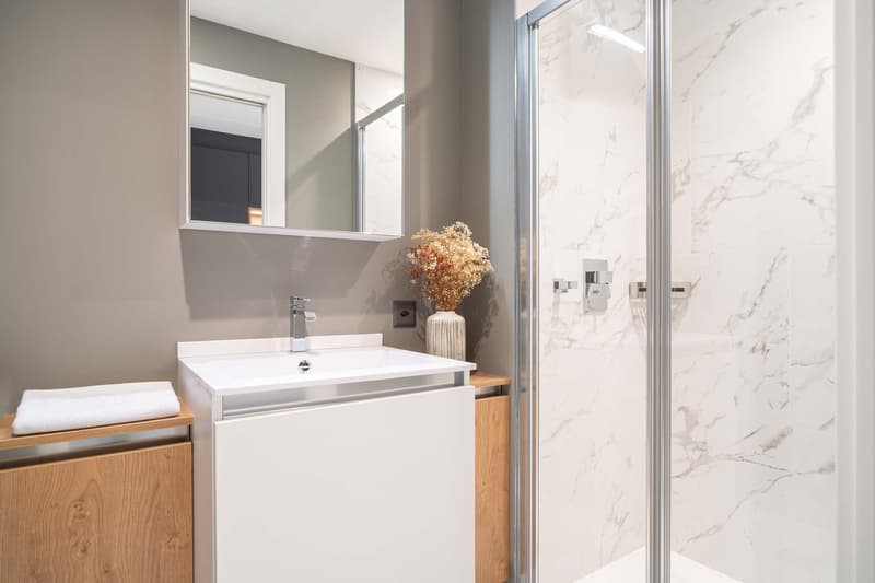 white shower stall, white sink, wooden cabinet, marble tiles