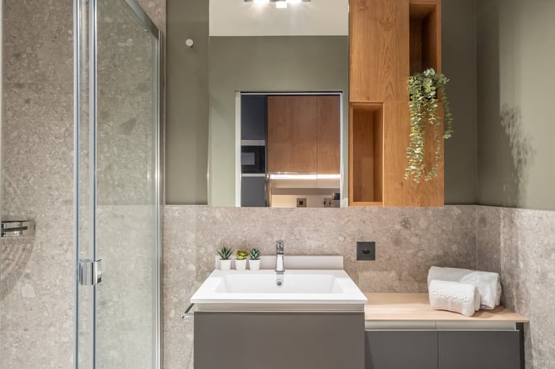 Modern bathroom with gray marble walls, white sink vanity, wooden shelving, and built-in appliances like a washing machine and dishwasher