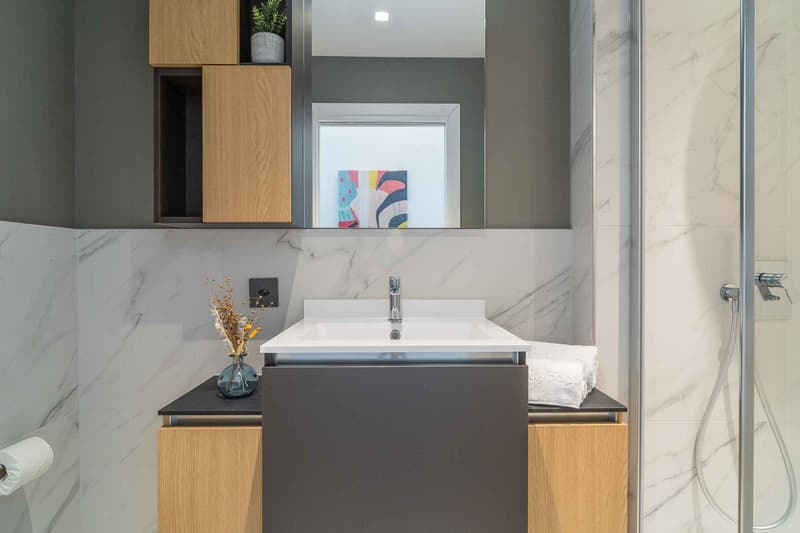 modern bathroom, marble tiles, white sink, wooden cabinets, shower enclosure, mirror, power outlet, toilet paper holder