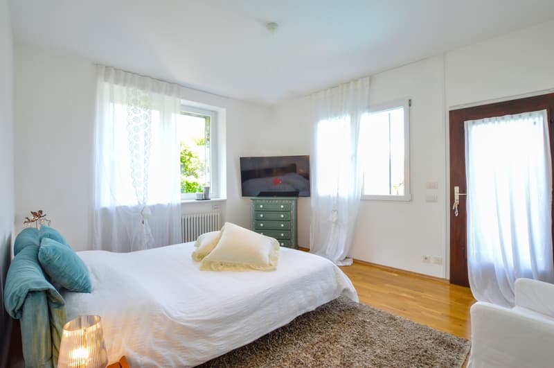 Das grosszügige Schlafzimmer mit mehreren Fenstern und Einbauschränken hat auch einen Zugang zur Terrasse. / La spaziosa camera con diverse finestre e un armadio a muro dispone anche di un'uscita su