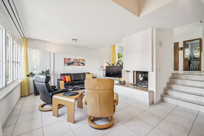 Wohnzimmer in Split-Level-Bauweise mit Cheminée. / a white living room with a large fireplace and modern furniture