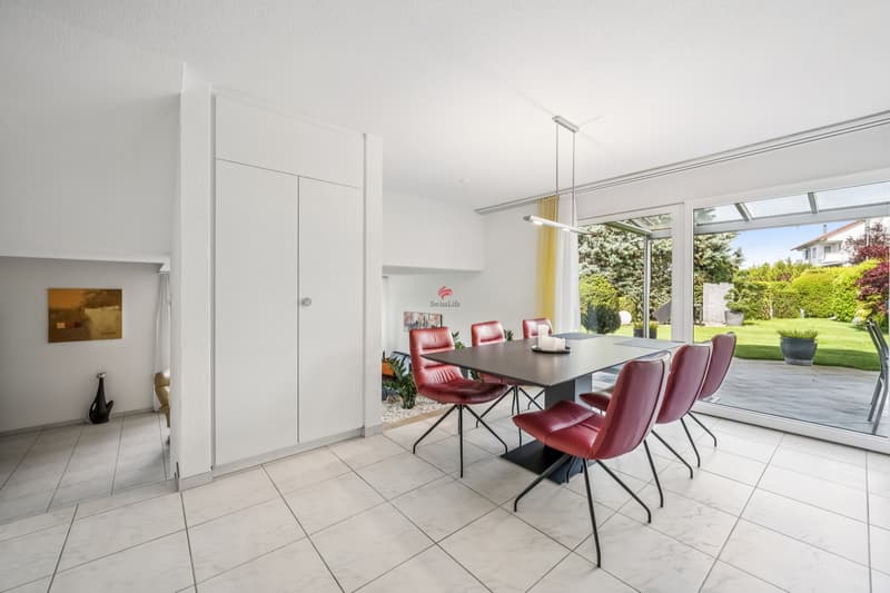 Modernes, helles Esszimmer mit direktem Zugang zum Garten. / a picture of a modern home with a dining table and red chairs in a room with a large sliding glass door that leads to a garden