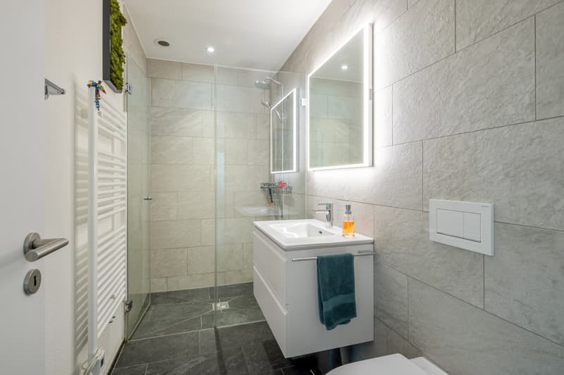 Modernes Badezimmer mit begehbarer Dusche und großen hellbeigen Natursteinoptik-Platten in warmem, elegantem Spa-Design