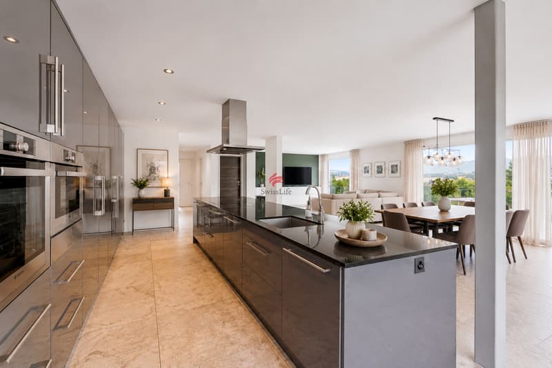 Das elegante Wohnkonzept vereint Kochen, Essen und Wohnen zu einem harmonischen Lebensraum mit zeitloser Architektur. Grosszügige Fensterfronten geben die Sicht ins Grüne frei und verleihen diesem B