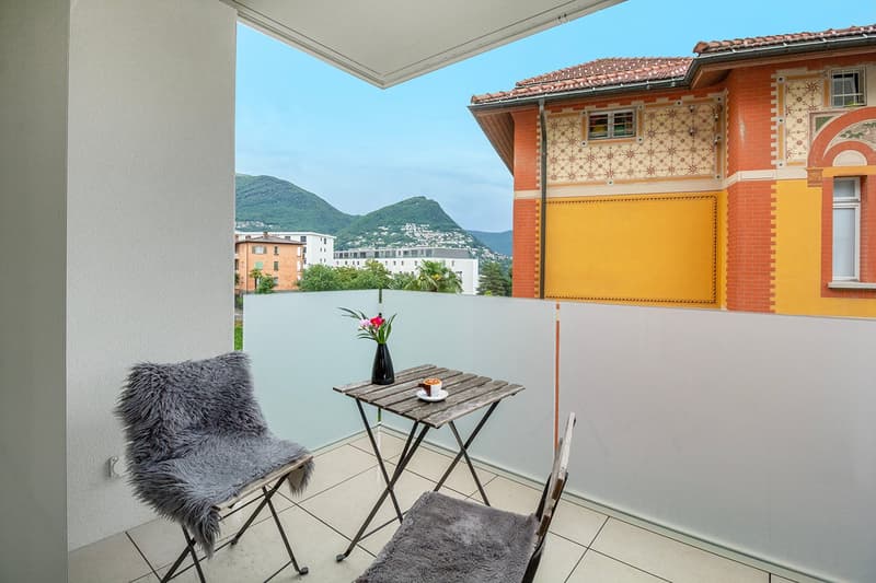 Balcony with tiled floor, two chairs with fur covers, a small table, vase with flowers, cup and saucer