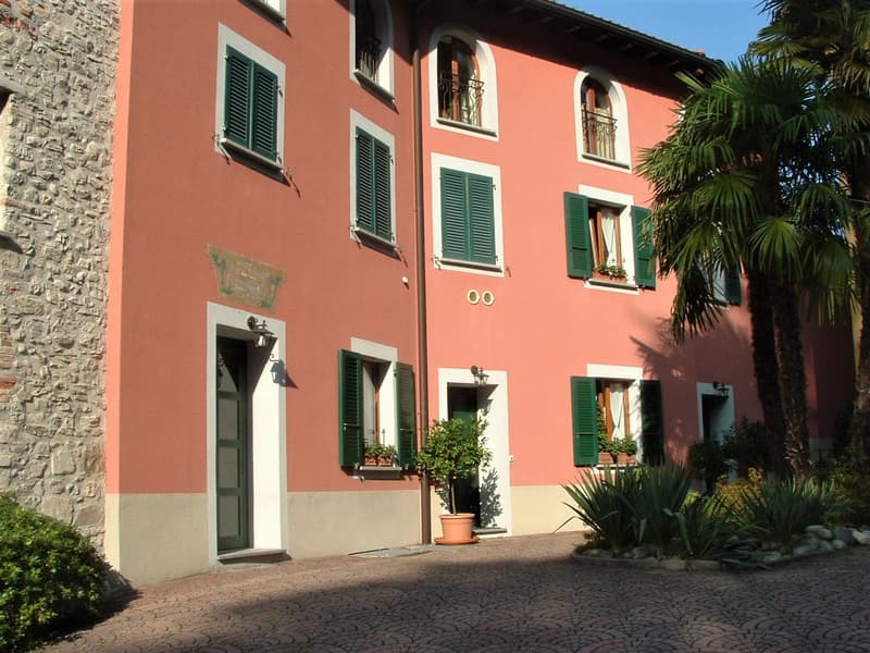 2 story house, red brick, white windows, green shutters, brown door, garden, plants, cobblestone road