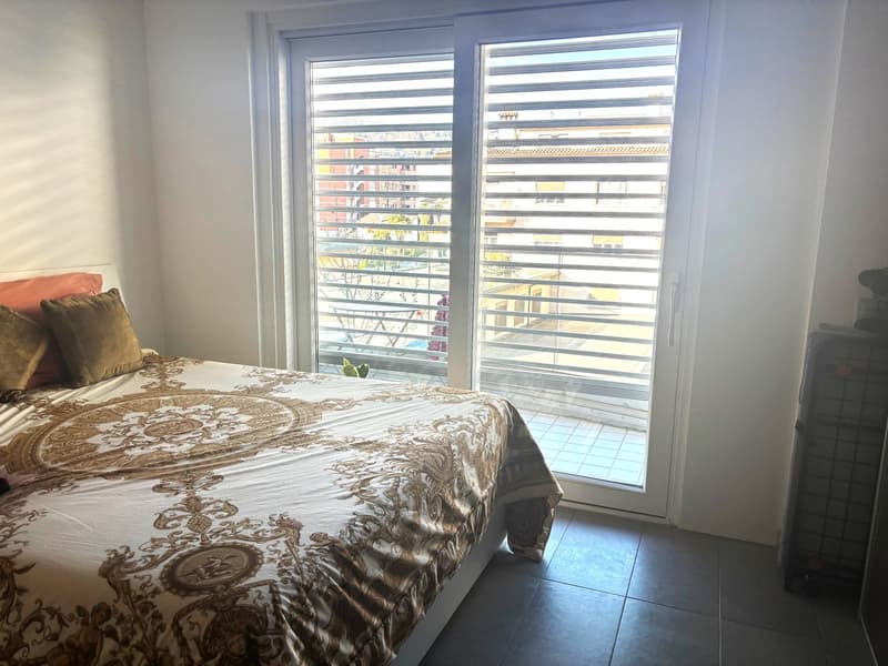 Bed with decorative pillow, sliding door with glass window, city view outside, tiled floor