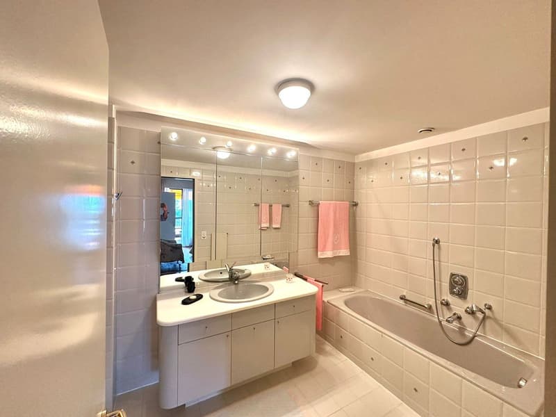 Large mirror, bathtub, sink, cabinet, tiled walls, ceiling light