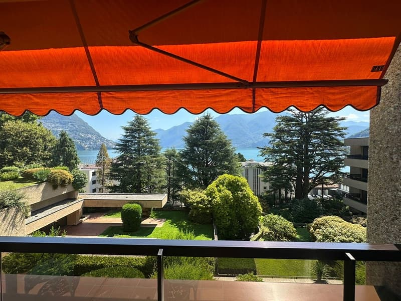 Balcony with panoramic view, trees, mountains and water, modern awning, garden with shrubs and lawn