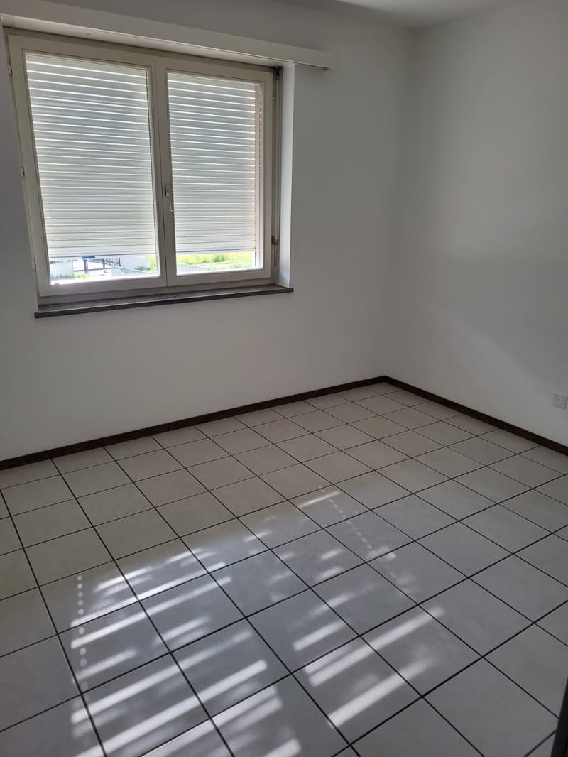 Empty room with white walls, gray tile flooring, and a window with horizontal blinds.
