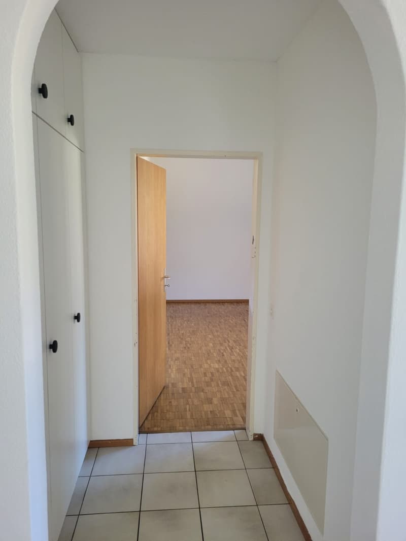 Empty hallway with tiled floor, open door, wooden floor, white walls