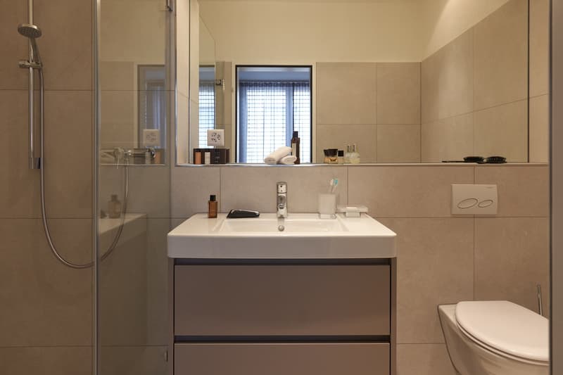 White sink, shower, tiled wall, mirror, power outlets, shampoo, conditioner, lotion
