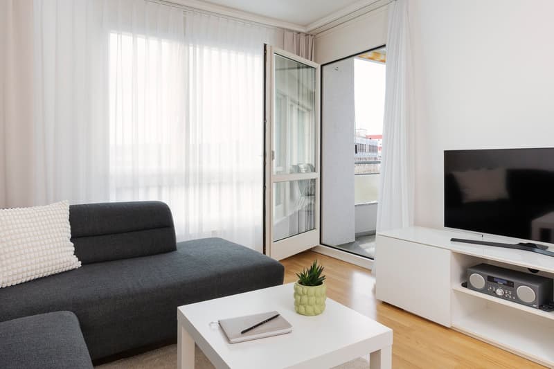 gray sofa, white coffee table, white curtains, glass door to balcony, television