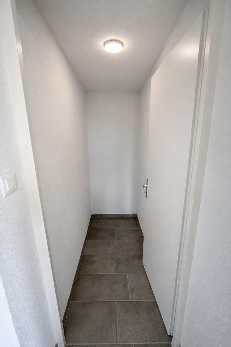 Empty hallway, white walls, beige tile flooring, ceiling light