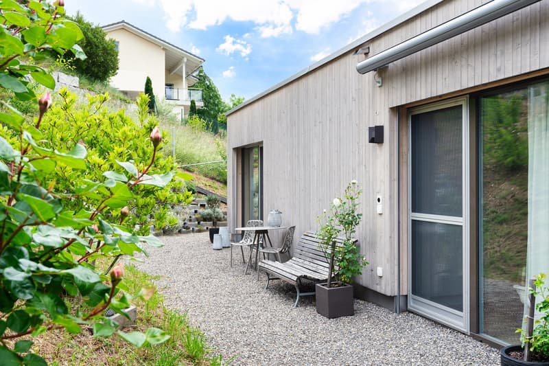 modern house, wooden exterior, gravel pathway, outdoor seating, glass doors, plants