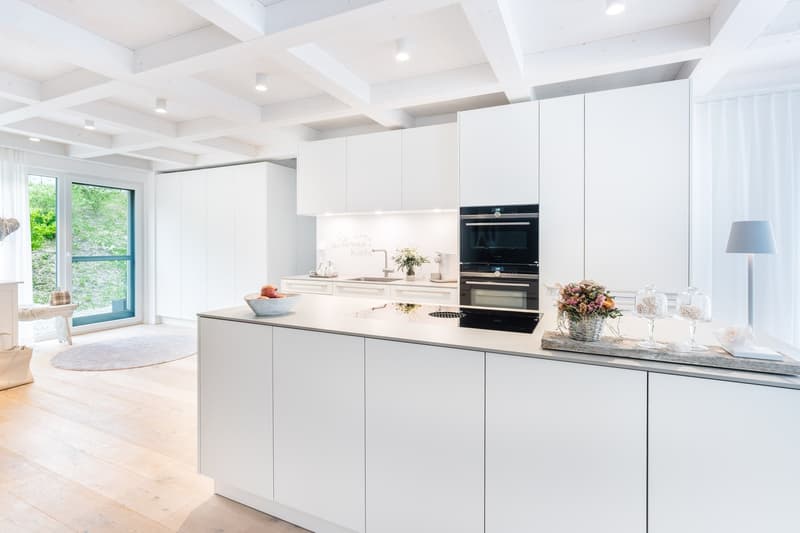 modern kitchen with white cabinets, wooden floor, large windows, island with sink and stove, decorative items