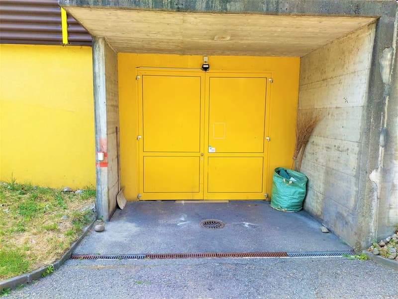Closed yellow doors, concrete walls, drain grate, green trash bag, brush