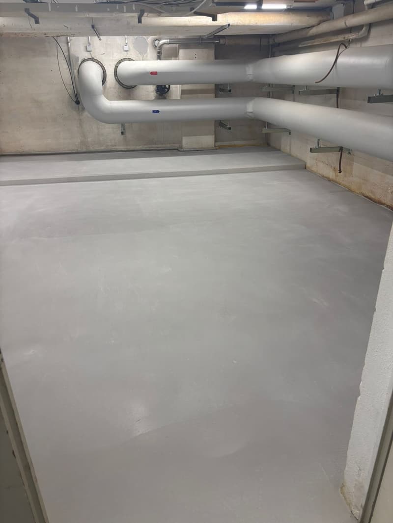 Concrete floor, white pipes, metal brackets, electrical wires, concrete walls