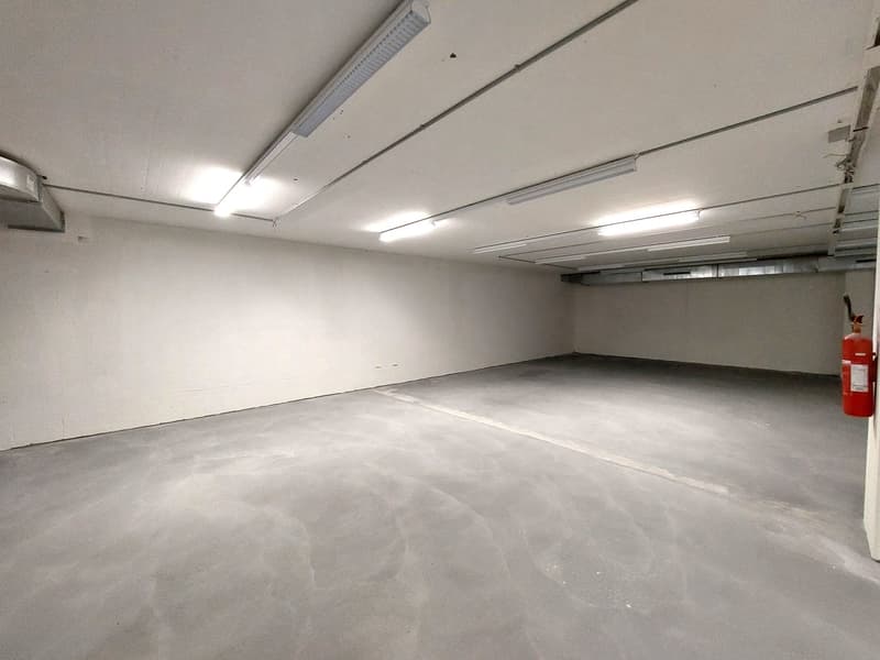 Empty parking lot, white walls, gray floor, fluorescent lights, fire extinguisher