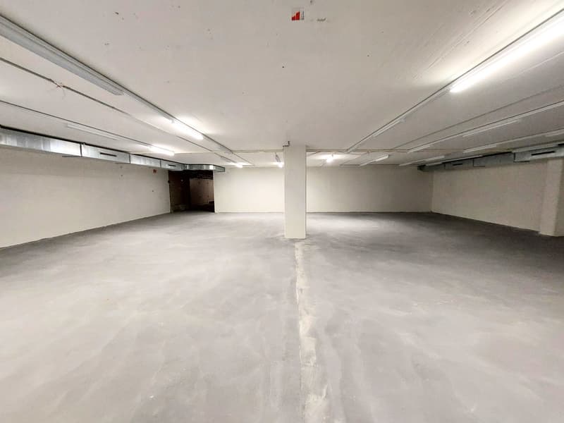 Empty parking area with white walls and ceiling, concrete floor, and fluorescent lights