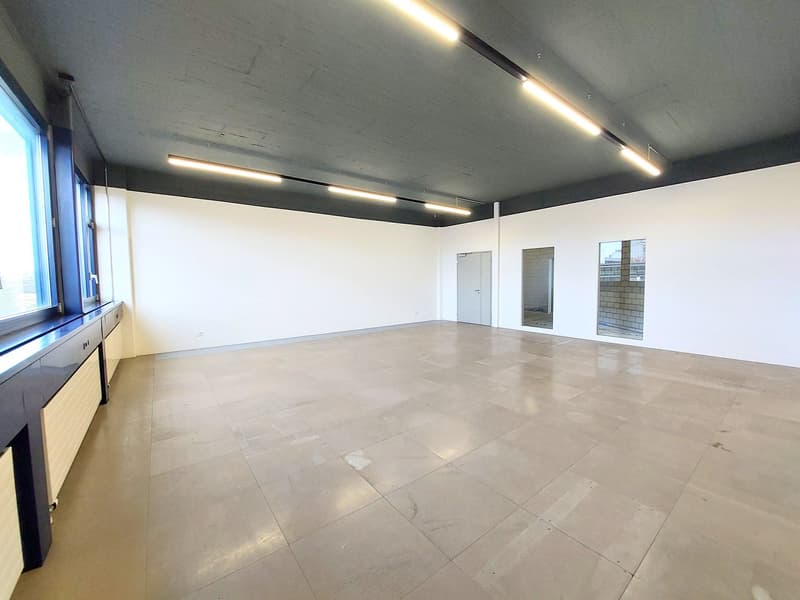 Empty room with white walls, tiled floor, large windows, and ceiling lights
