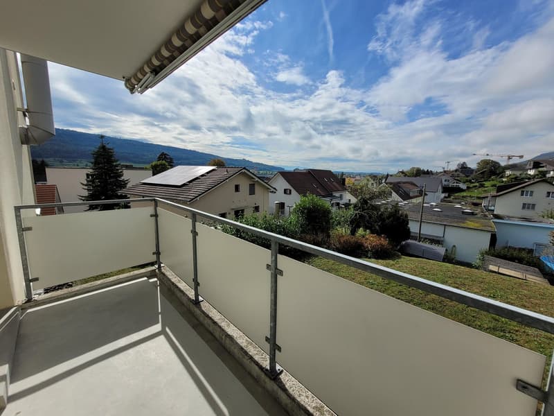 A balcony with a railing and glass panel, offering a scenic view of houses and a mountain in the background.