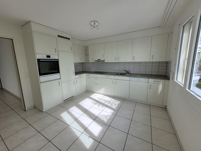 Fully equipped modern kitchen with white cabinetry, white tiled floor, oven, dishwasher, sink, countertops, lighting, and windows.