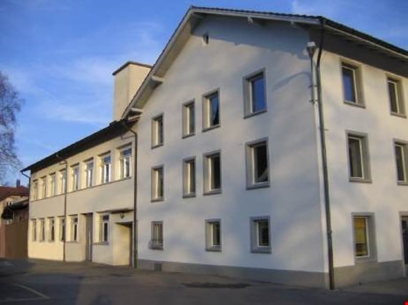 2 story building, white exterior, multiple windows, flat roof, entrance on the left side