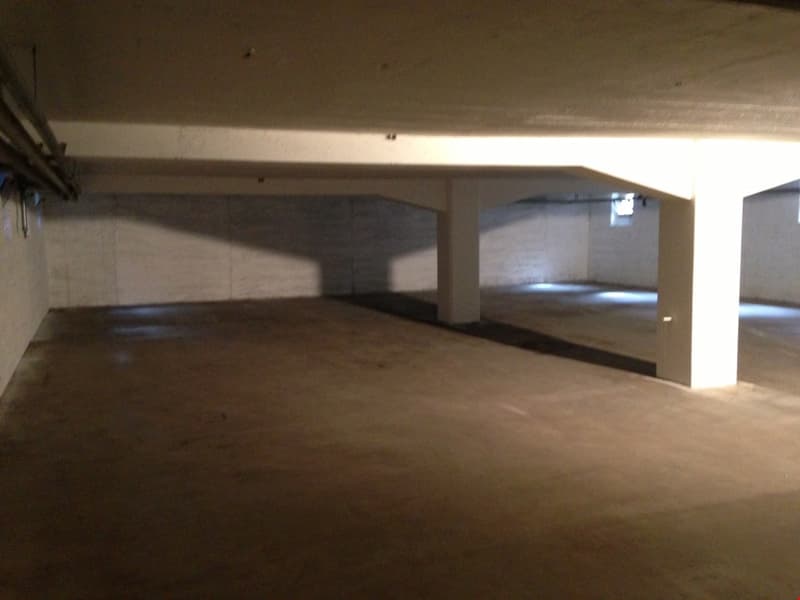 Large empty parking space with exposed ceiling beams and concrete floor.