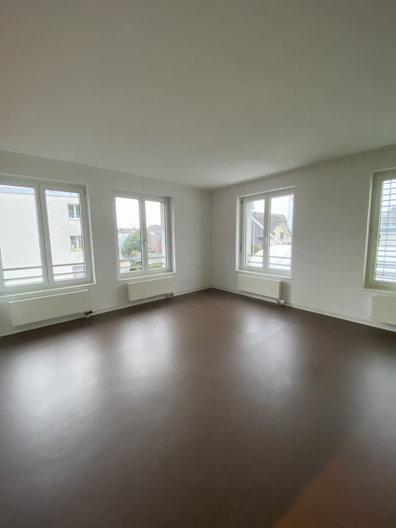 Empty room with white walls, brown floor, three windows, and radiators