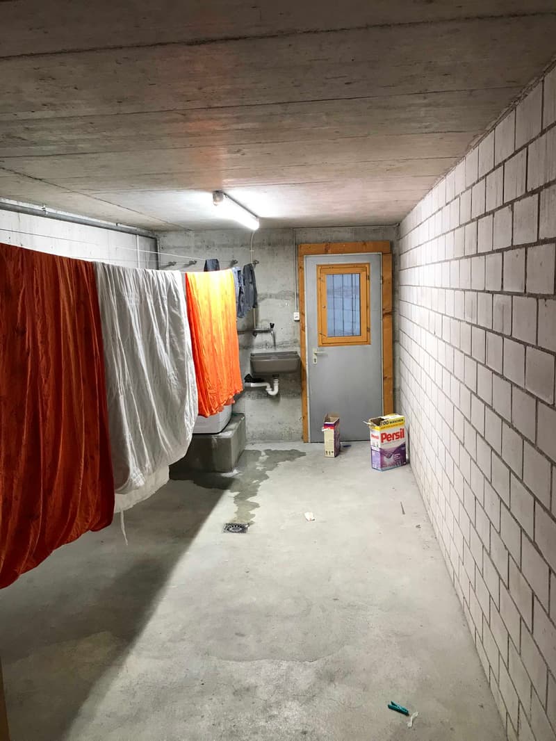 Concrete walls, concrete floor, clothes hanging on drying rack, sink, washing machine, Persil detergent