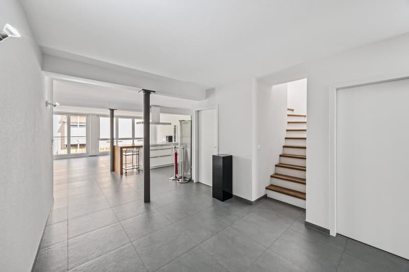 Entrance hall with stairs, wooden steps, large windows, kitchen area, tiled floor.