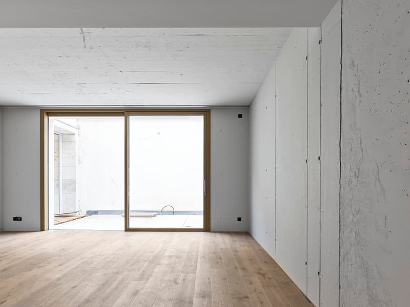 Large open space with white walls, wooden floor, and sliding glass doors leading to a balcony or terrace