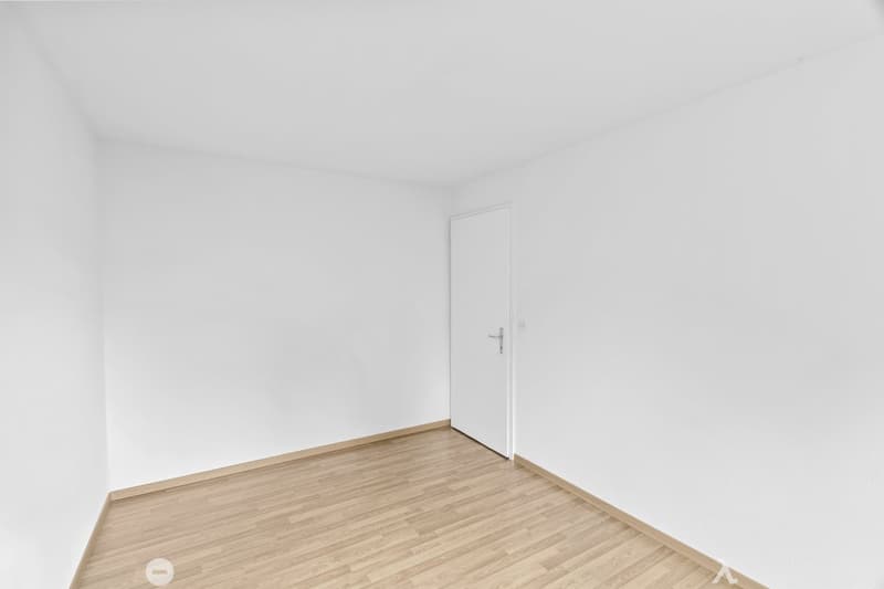 Empty room with white walls, wooden floor, and a white door.