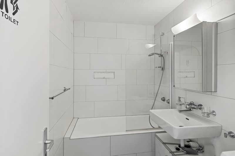 modern bathroom with white tiles, bathtub, shower, sink, mirror, and a glass door