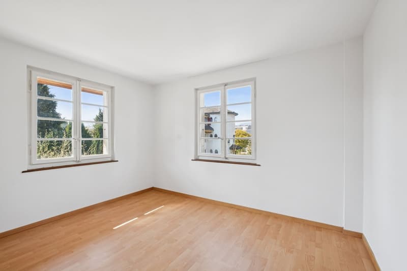 empty room, white walls, wooden floor, two windows with view of trees