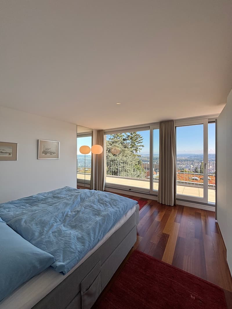 bedroom, double bed with blue blankets, two bedside lamps, wooden floors, balcony, large windows