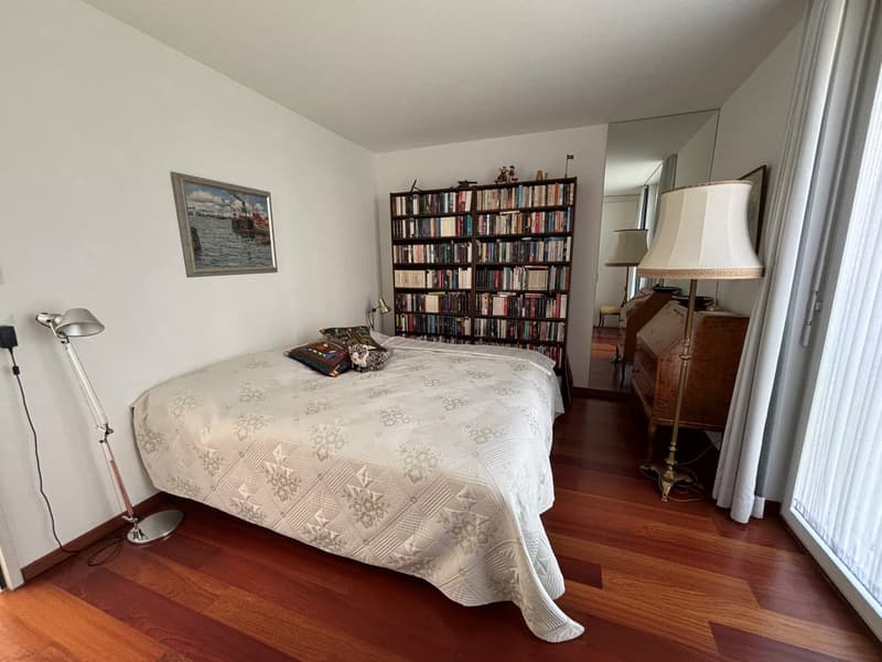 large bed, white bedding, floor lamp, bookshelf, wooden floor, painting, desk, mirror, window