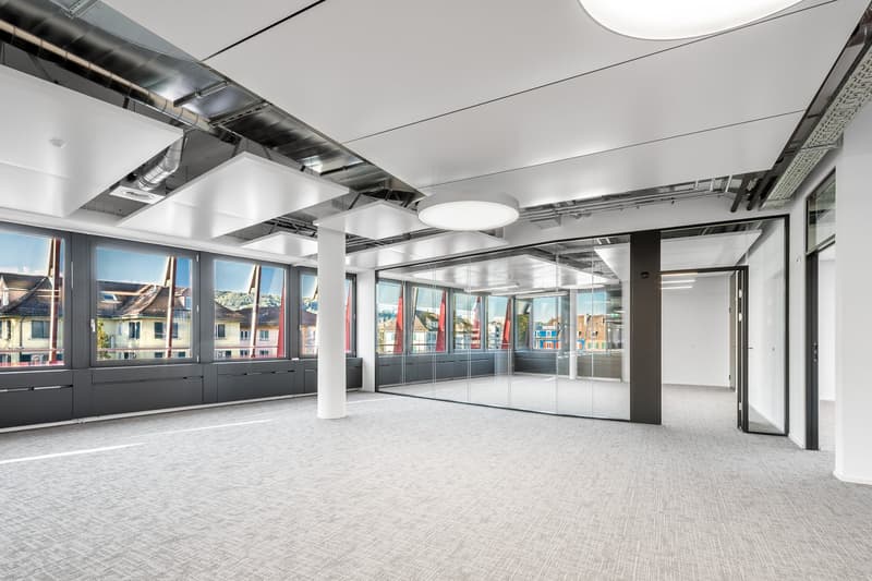 An empty office with white ceiling, large windows with city view, glass wall, carpeted floor, pillar in the middle
