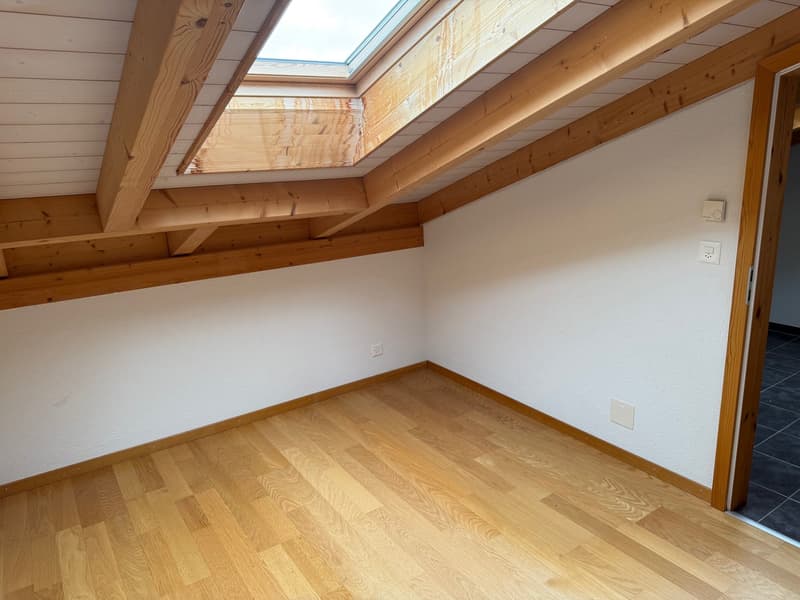 empty attic room, wooden floor, white walls, wooden beams, skylight, outlet, wall switch